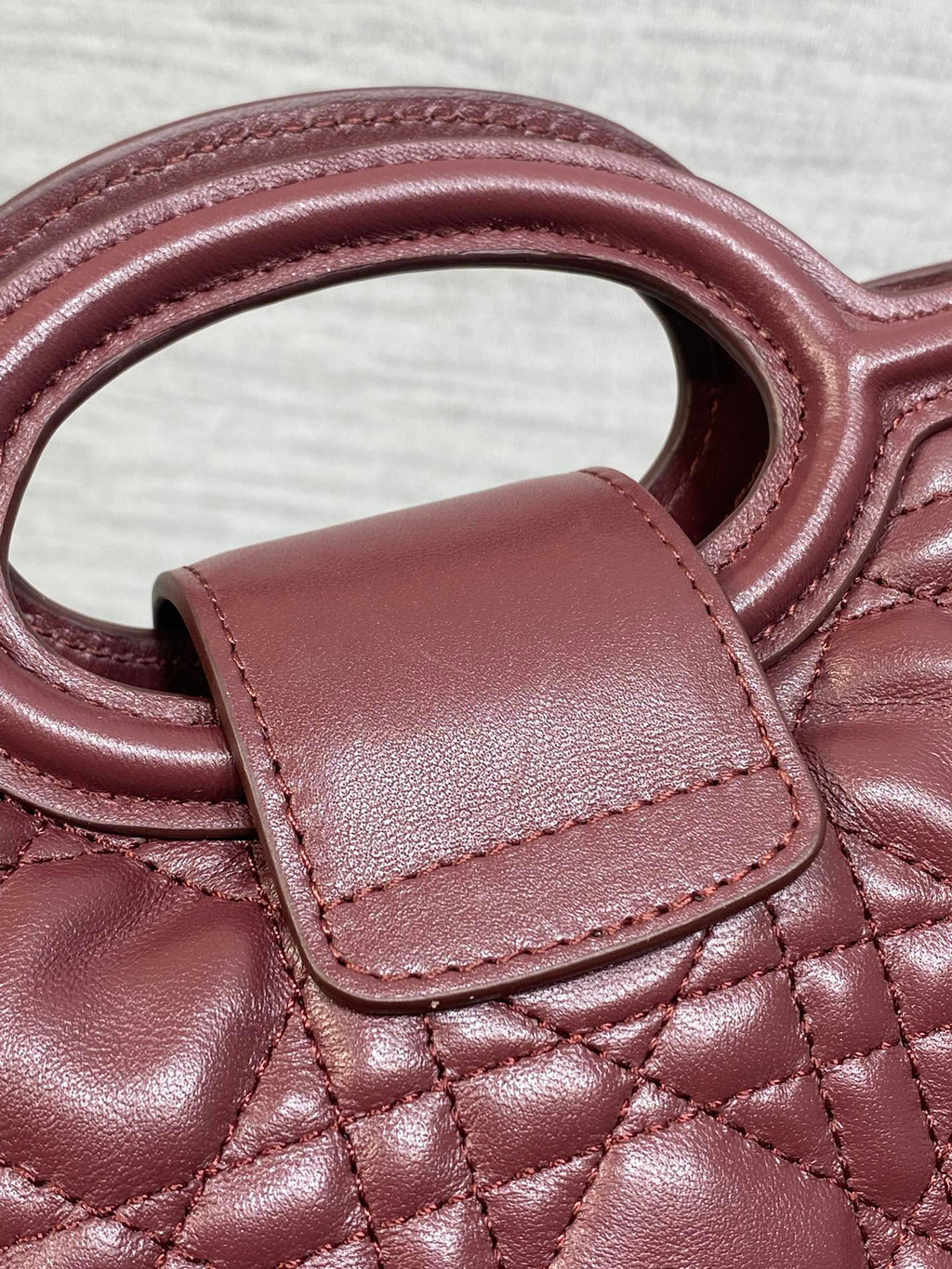 Maroon quilted handbag strap and top handle with leather tab and visible stitching