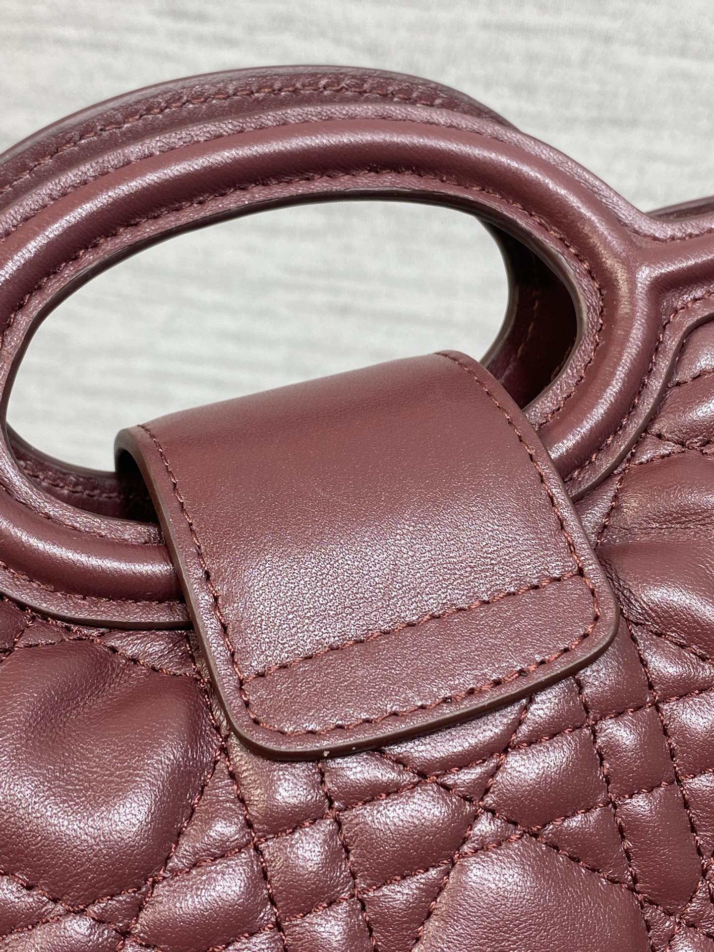 Maroon quilted handbag strap and top handle with leather tab and visible stitching