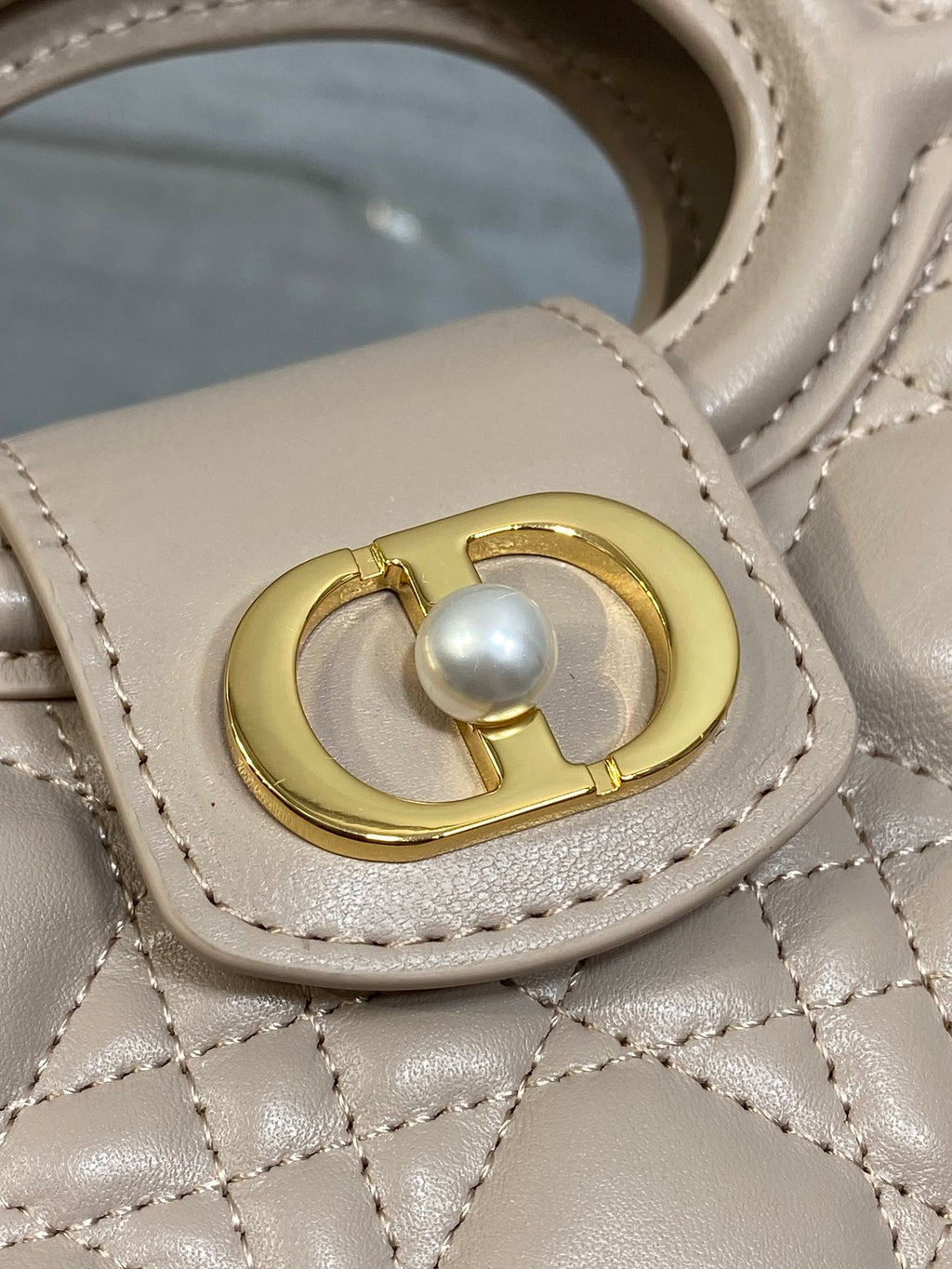Beige quilted handbag detail with gold ring clasp and pearl charm