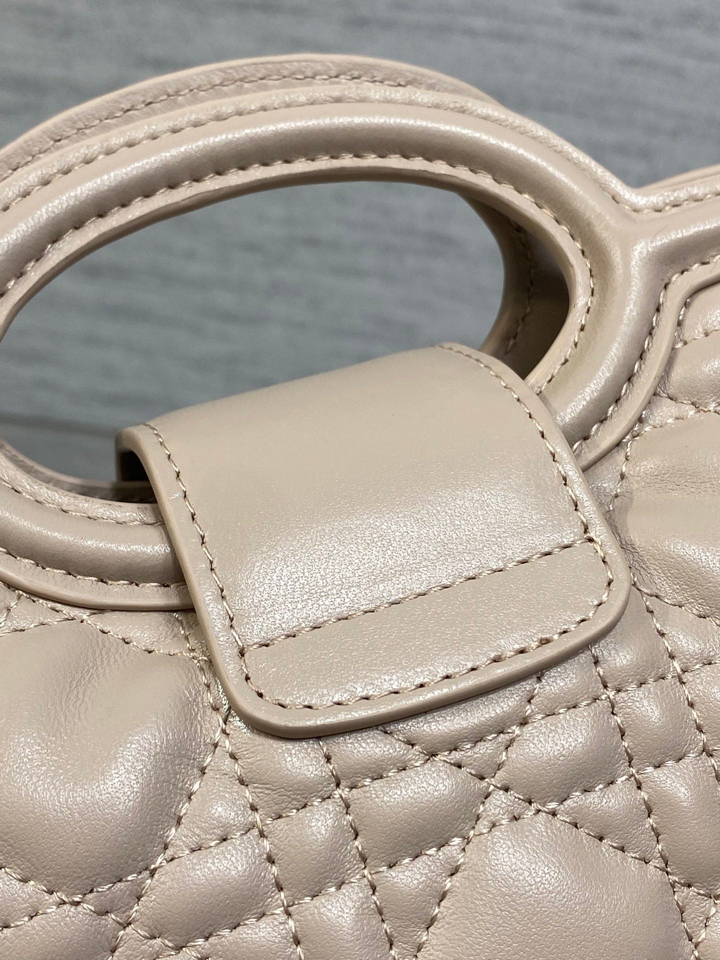 Beige quilted mini handbag front flap with stitched trim and strap
