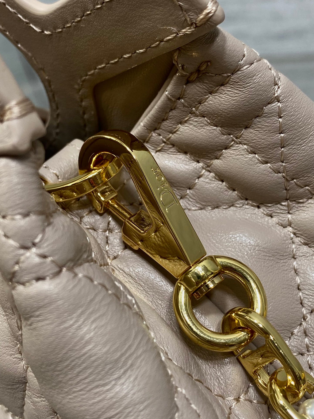 Beige handbag hardware closeup with gold-tone clasp and chain attachment