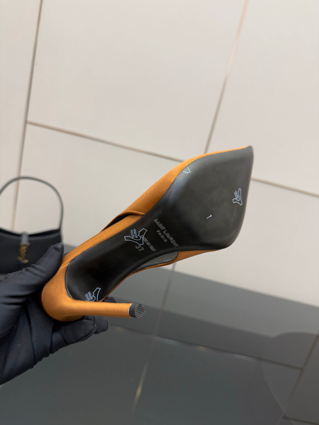 Orange pointed-toe high-heel pump held to show black outsole and heel