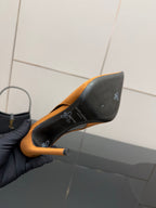 Orange pointed-toe high-heel pump held to show black outsole and heel