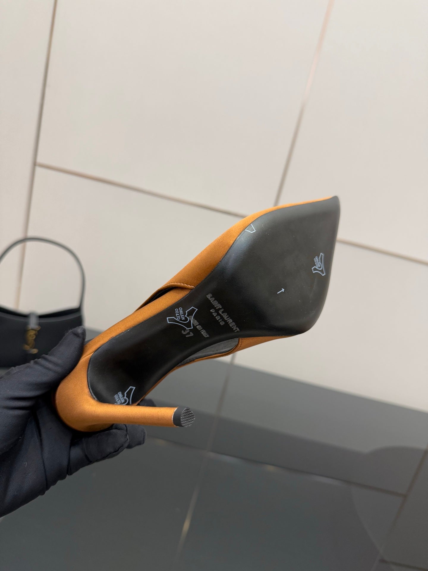 Orange pointed-toe high-heel pump held to show black outsole and heel