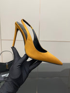 Yellow pointed-toe stiletto heel shoe held in black glove, showing side profile