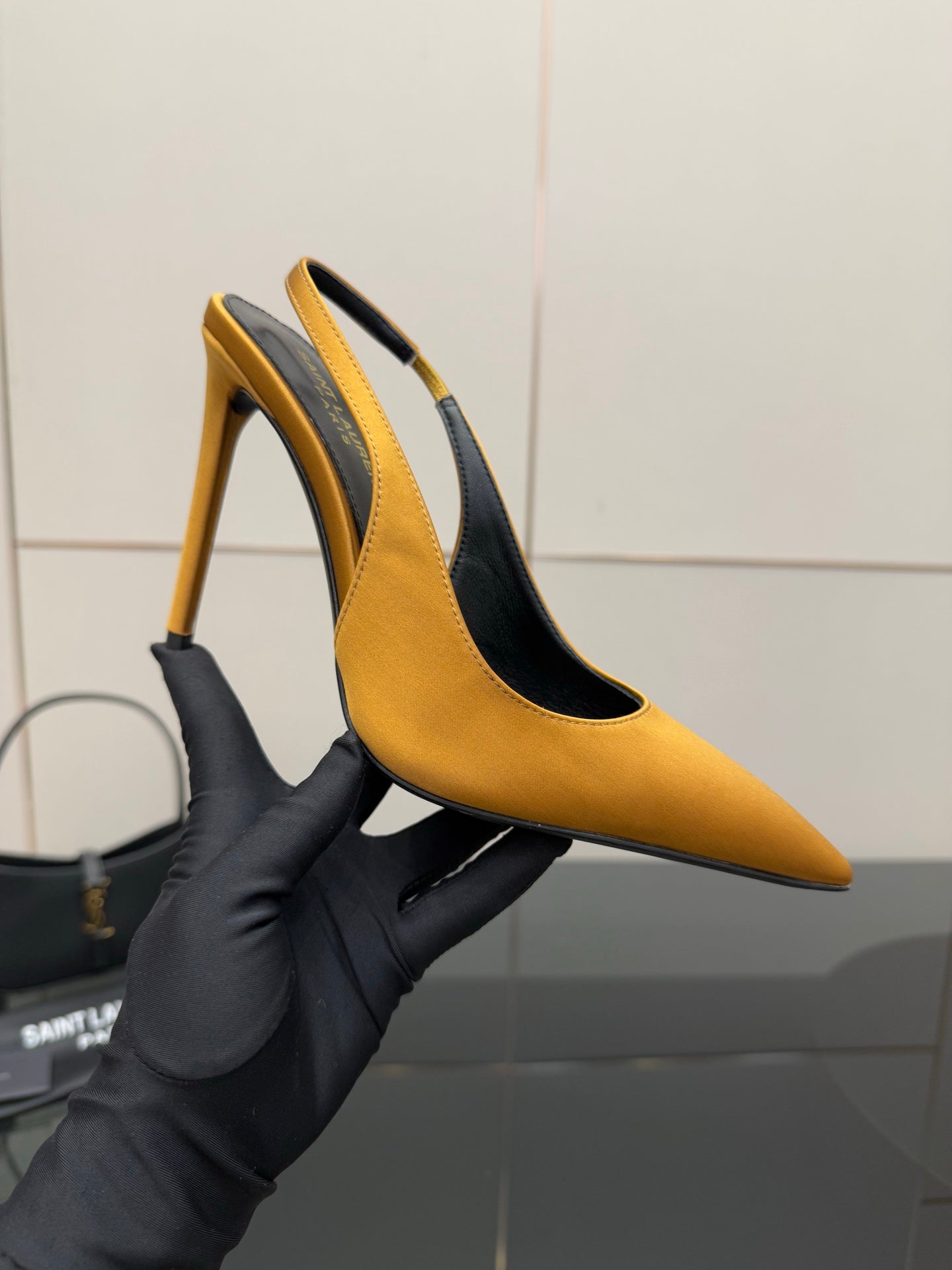 Yellow pointed-toe stiletto heel shoe held in black glove, showing side profile