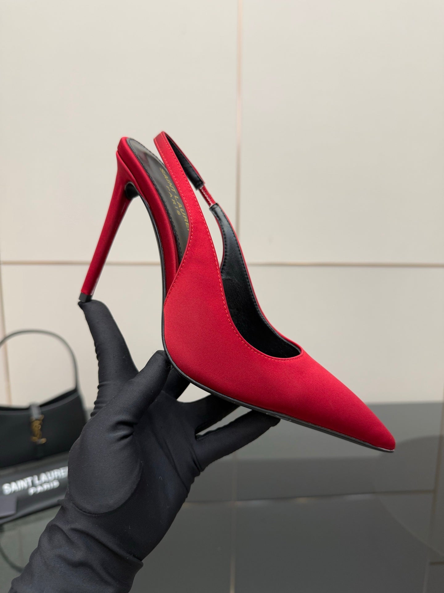 Ladies red pointed-toe stiletto pumps held in black glove, side view