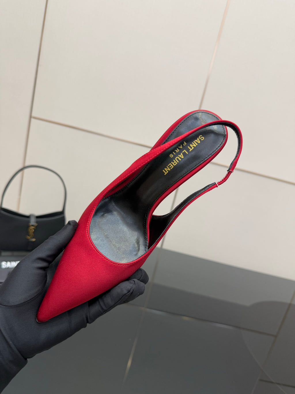 Ladies red high-heel pumps held in black glove, showing inner side