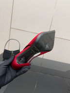 Ladies red pointed-toe stiletto pump held in black glove, side view