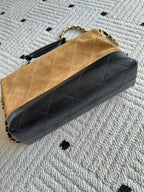 Designer handbag with tan top, black quilted body, and gold chain link hardware