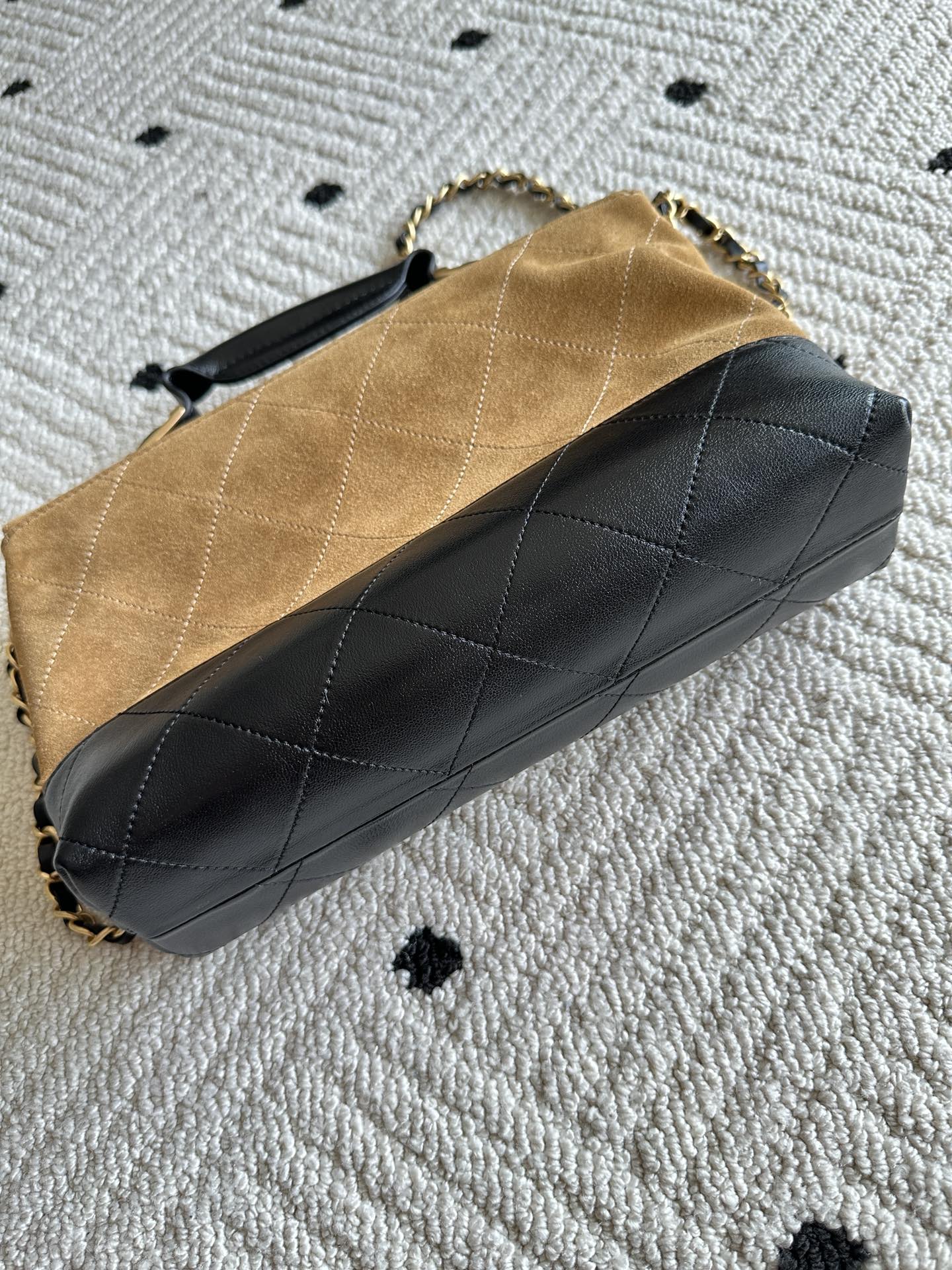 Designer handbag with tan top, black quilted body, and gold chain link hardware