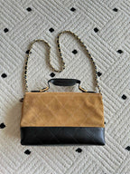 Designer handbag with tan flap, black quilted base, and gold chain shoulder strap