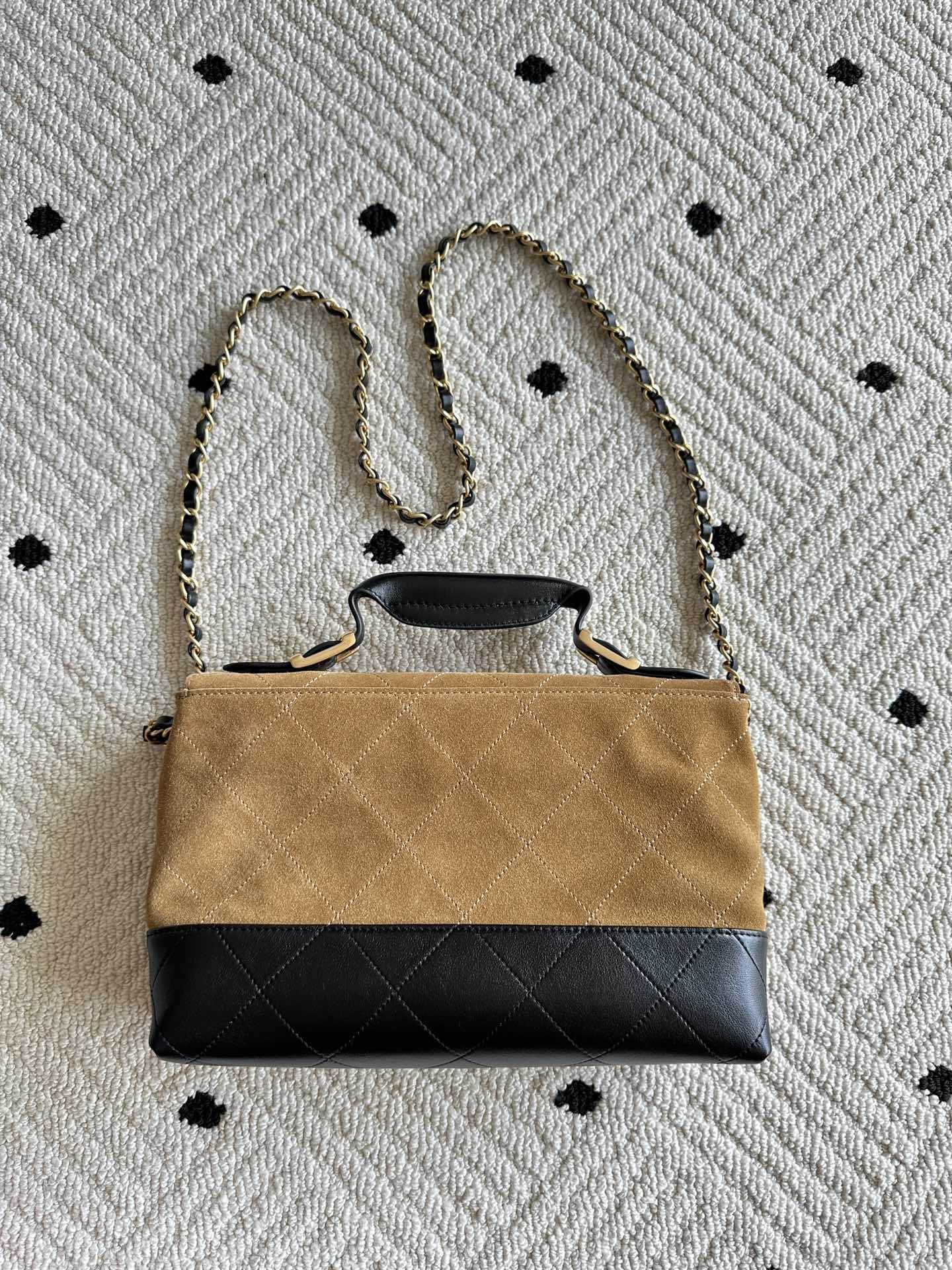 Designer handbag with tan flap, black quilted base, and gold chain shoulder strap
