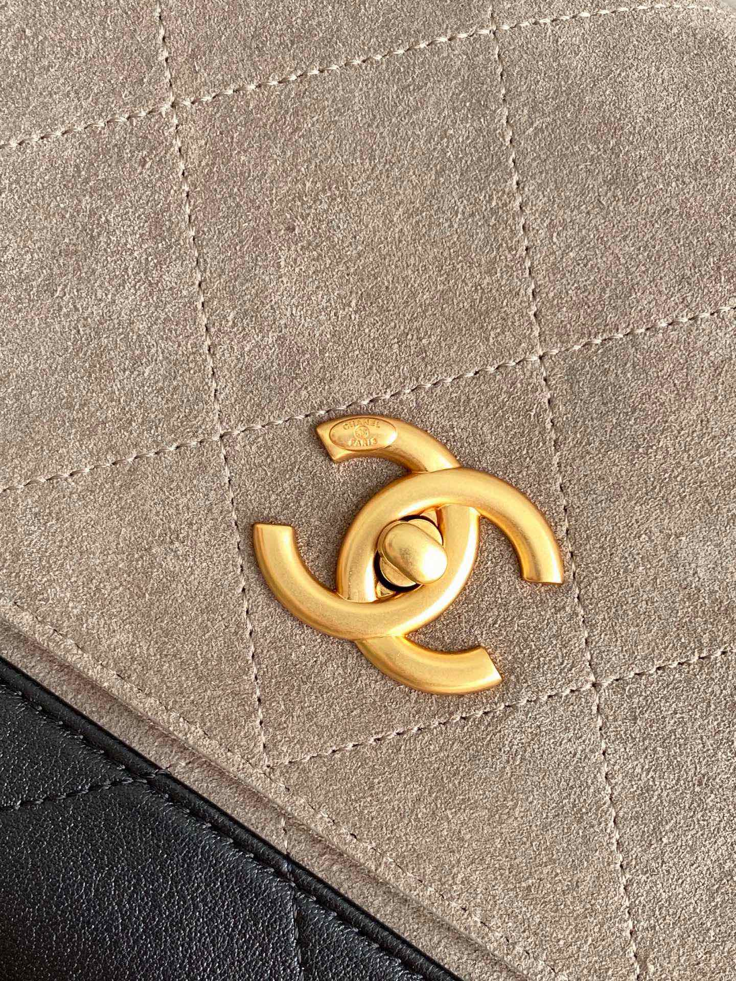 Chanel bag close-up of gold CC logo hardware on beige fabric