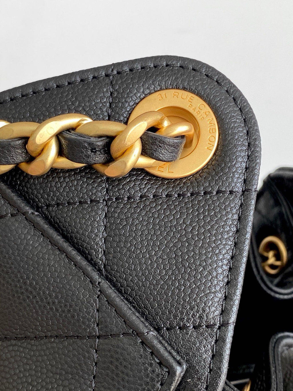 Chanel bag detail, gold chain and ring clasp on black leather flap