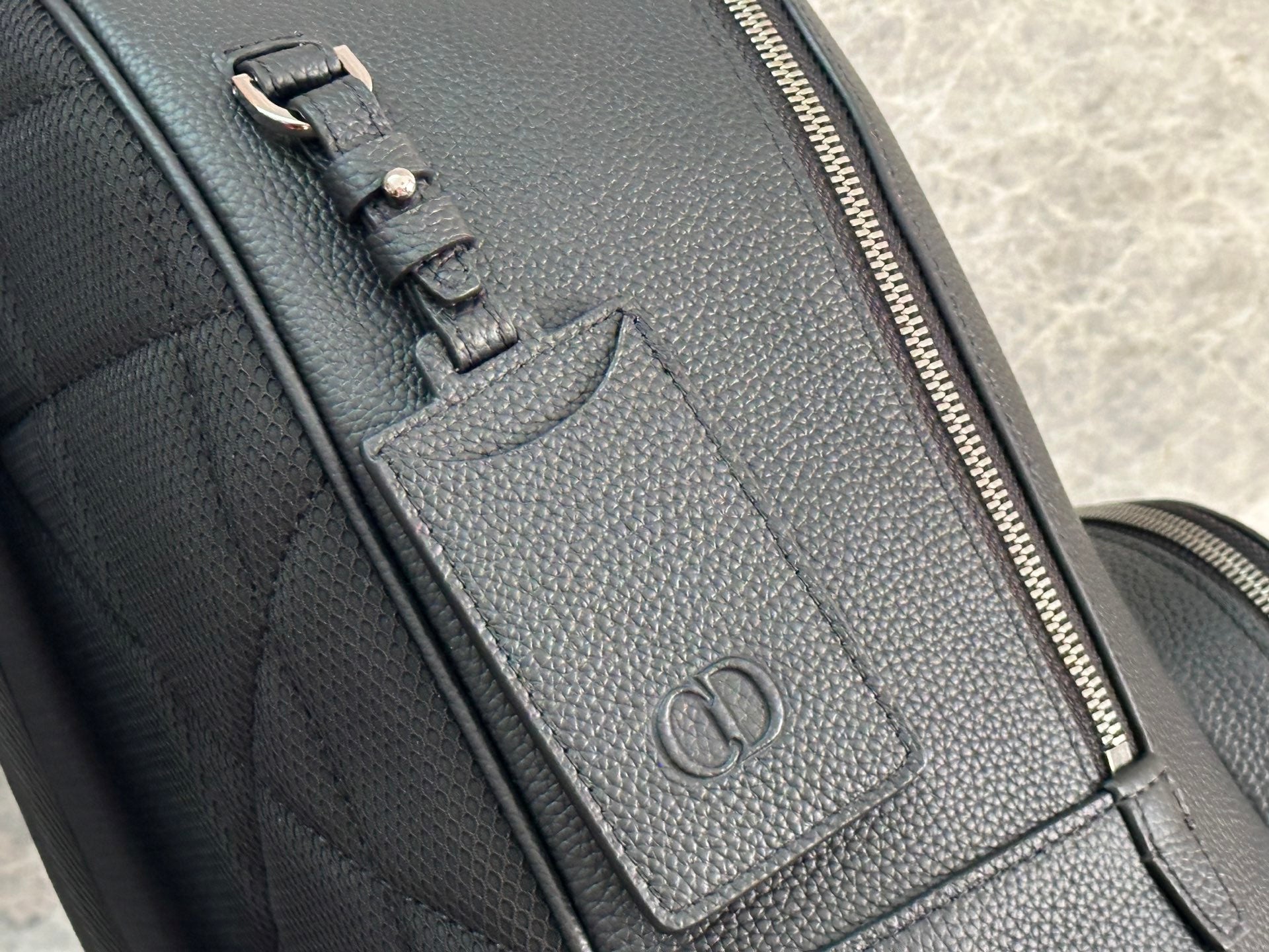 Close-up of dark green leather-look zipper track and embossed logo patch.
