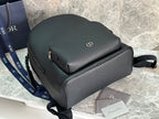 Dark green leather-look backpack with rounded top, front zip, and logo plaque detail.