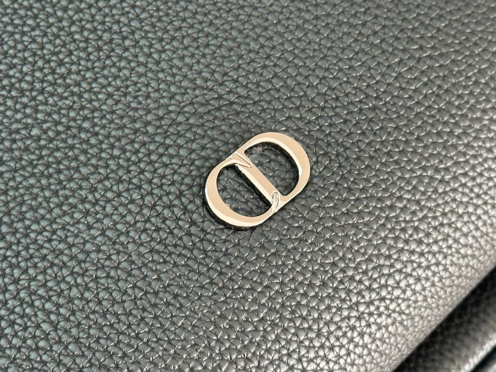 Close-up of gold-tone metal logo hardware on dark green pebbled leather-look.