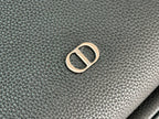 Close-up of gold-tone metal logo hardware on dark green pebbled leather-look.