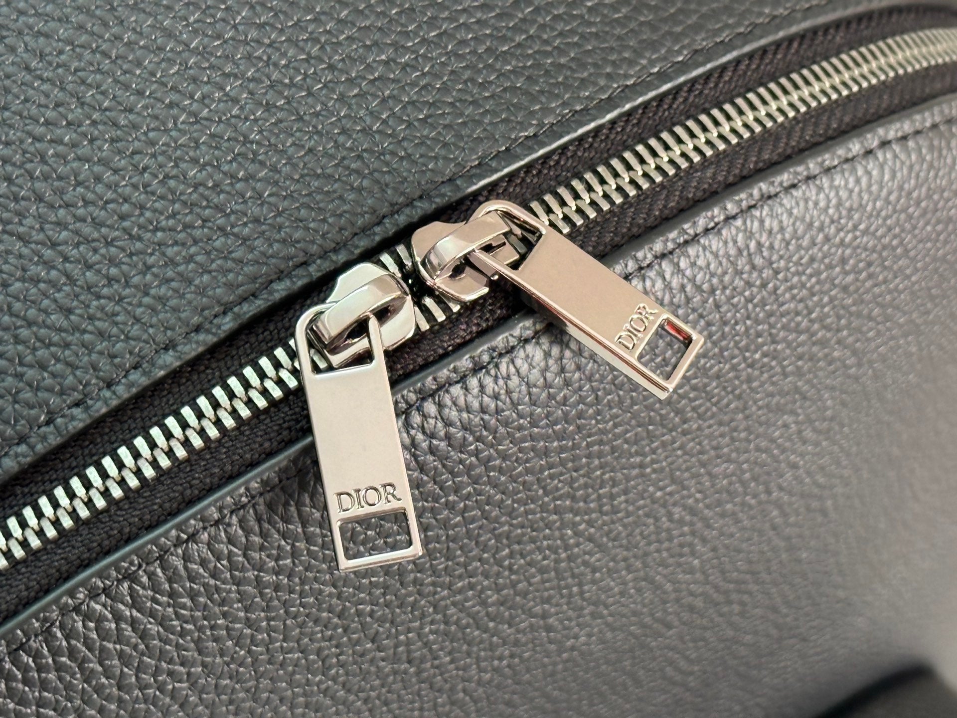 Close-up of silver-tone zipper and metal zipper tags on dark green bag.