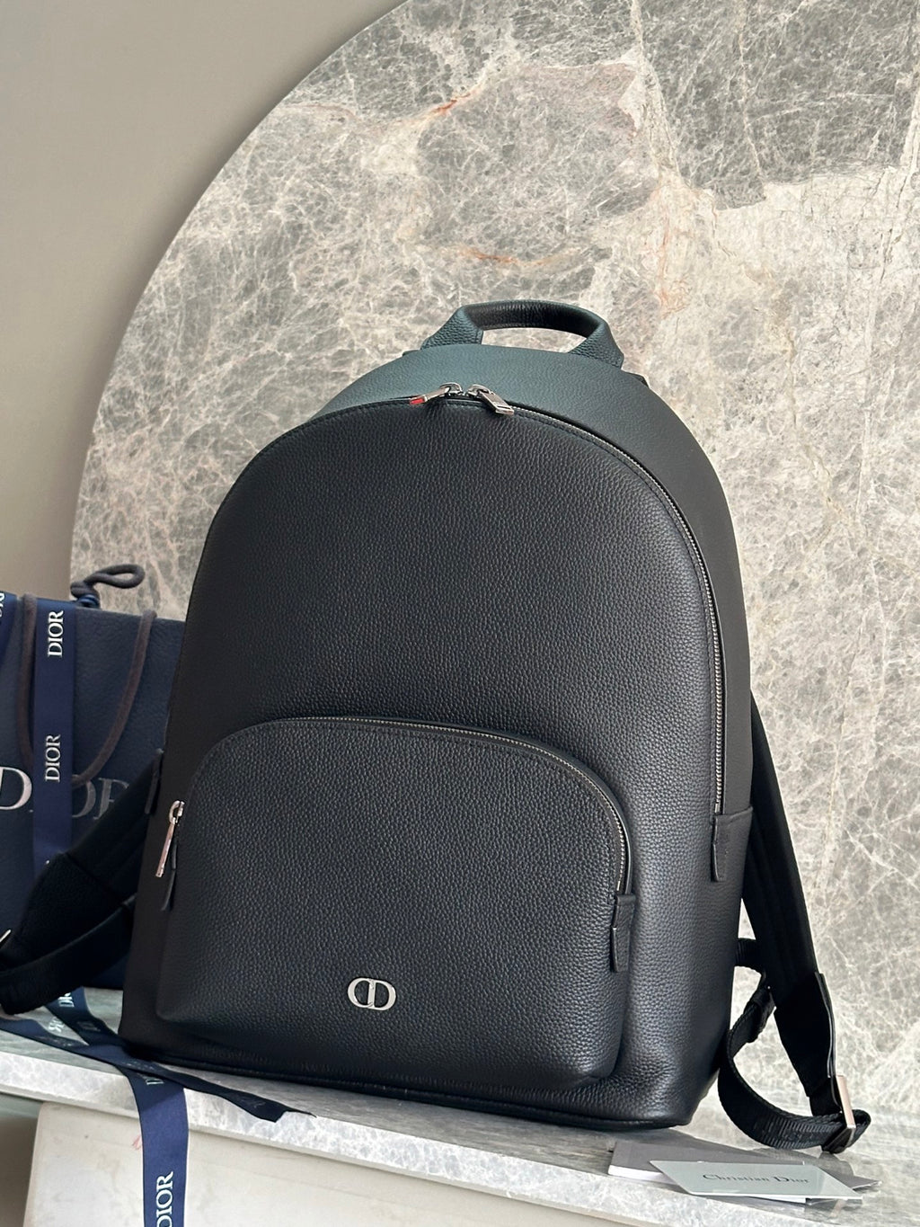 Dark green leather-look backpack with top handle, front pocket, and small logo emblem.