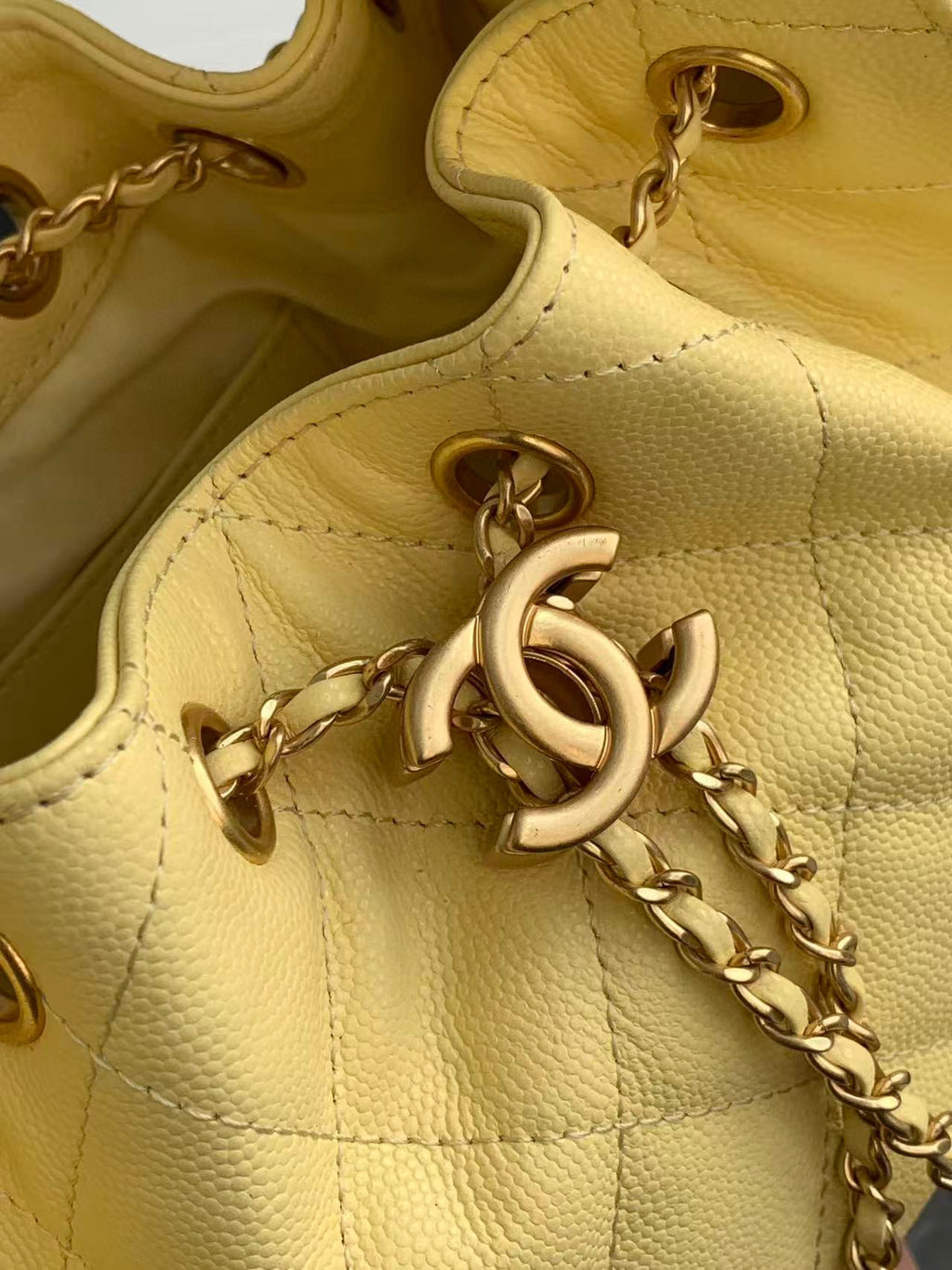 Pale yellow leather bag detail with gold-tone ring hardware and chain strap.