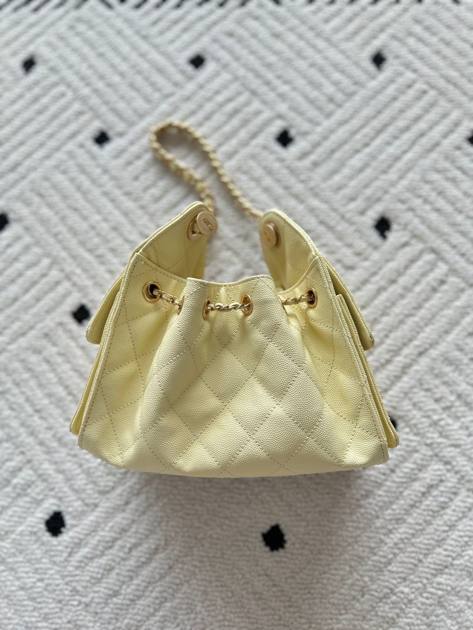 Bucket-style handbag in pale yellow with quilted sides and gold chain handles.