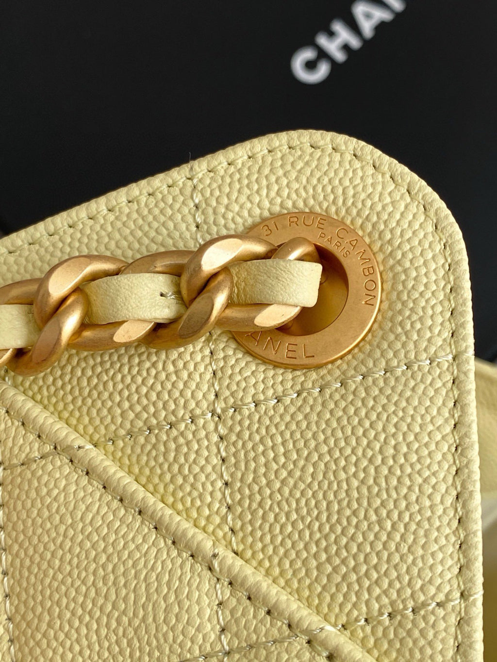Pale yellow leather bag with circular gold logo medallion and chain link.