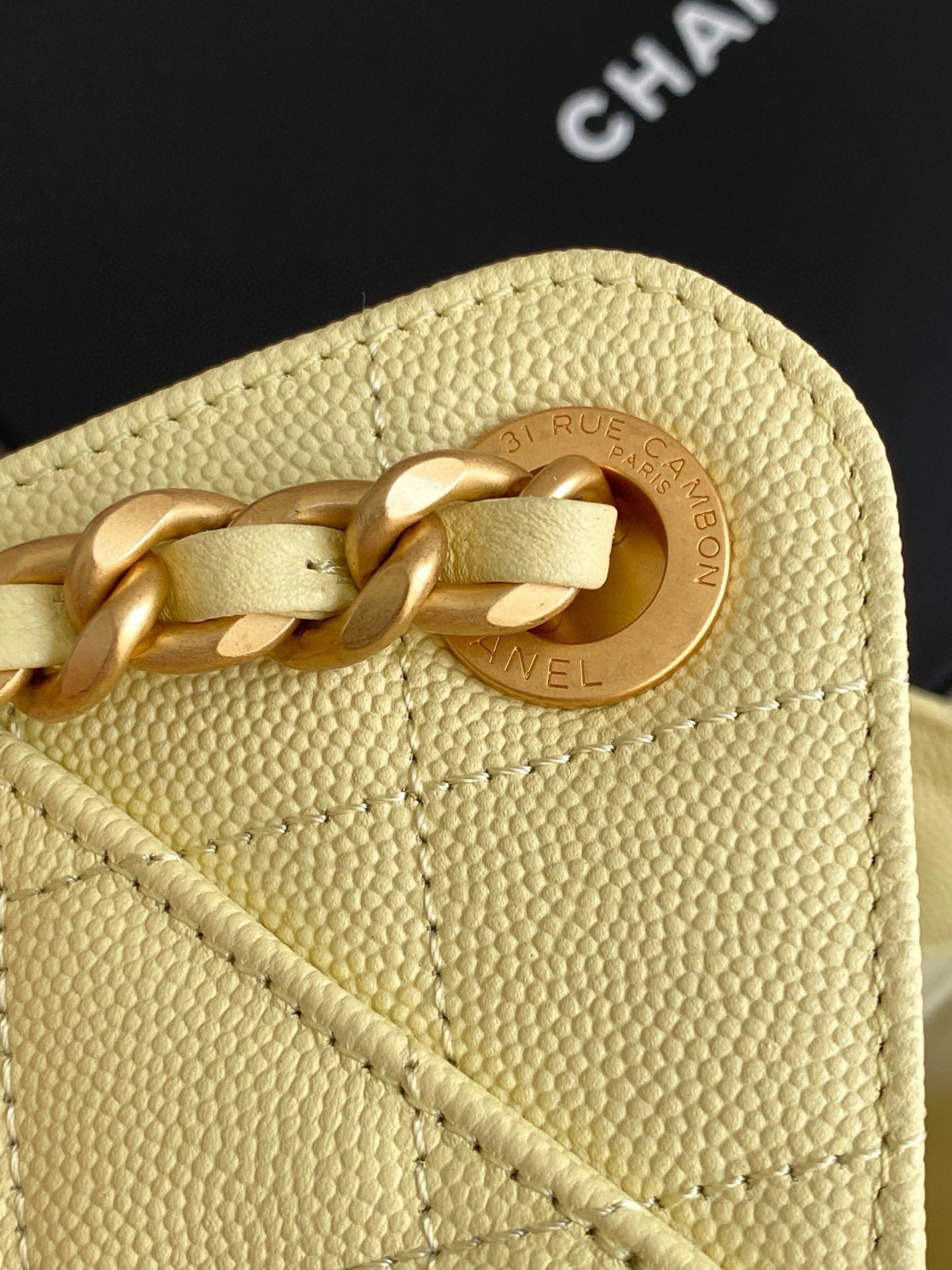 Pale yellow leather bag with circular gold logo medallion and chain link.