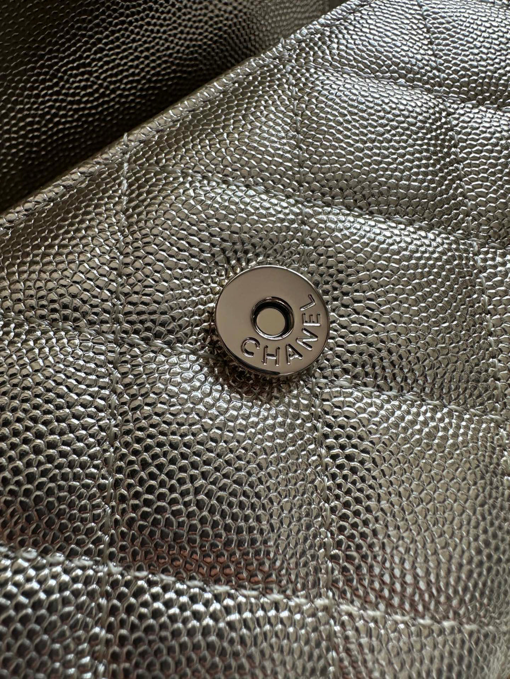 Chanel bag front logo medallion on textured metallic surface