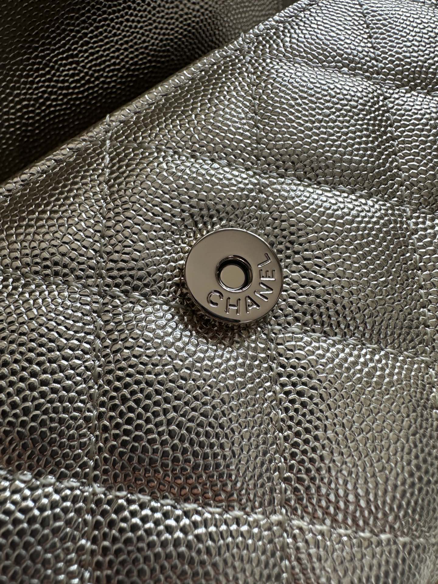 Chanel bag front logo medallion on textured metallic surface