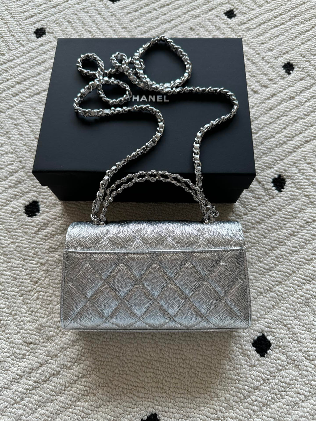 Light silver quilted flap bag with chain strap, front logo detail, and short handle