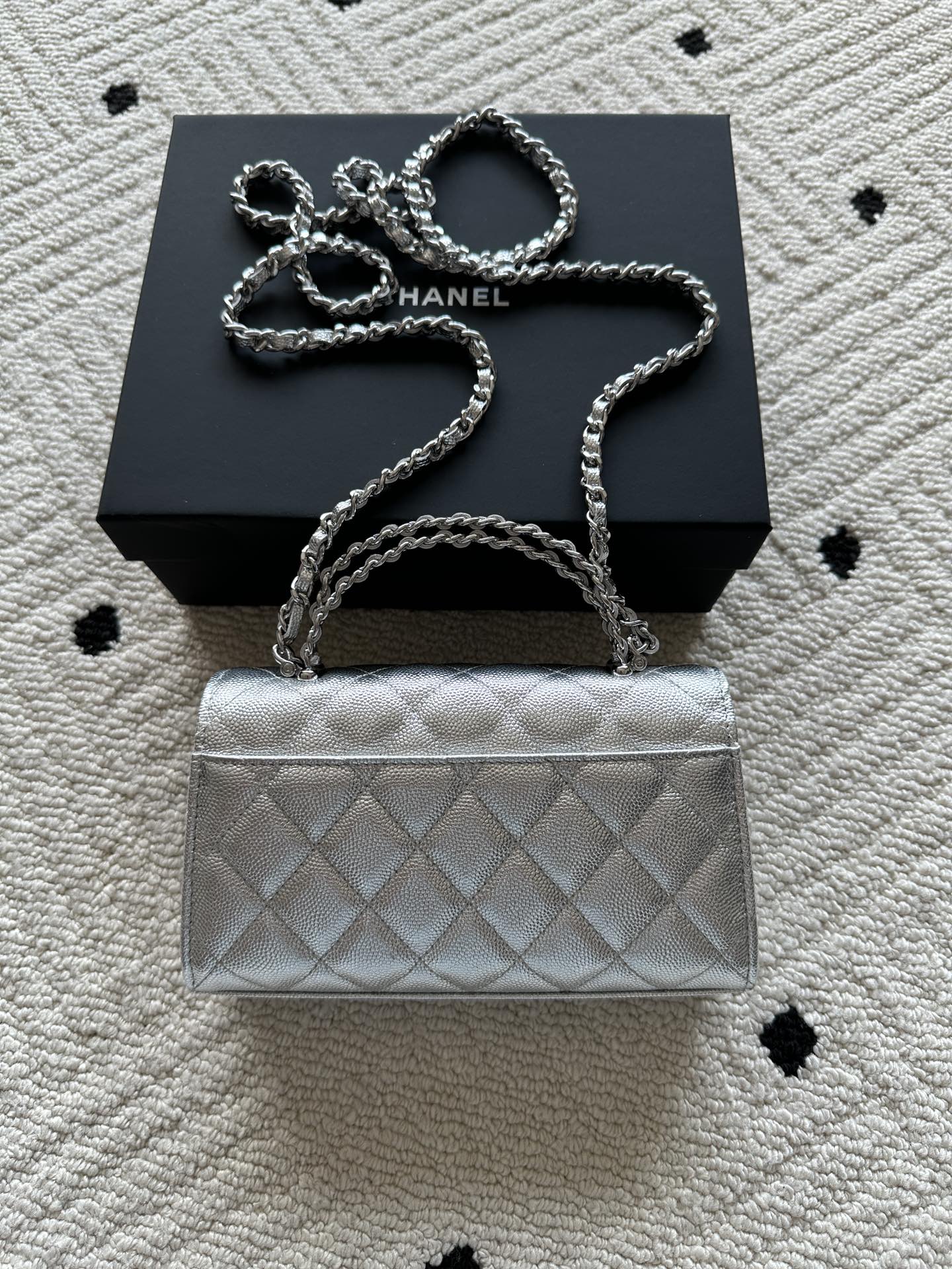 Light silver quilted flap bag with chain strap, front logo detail, and short handle