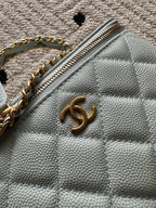 Light-blue quilted mini bag with gold-tone logo on flap and top zipper detail