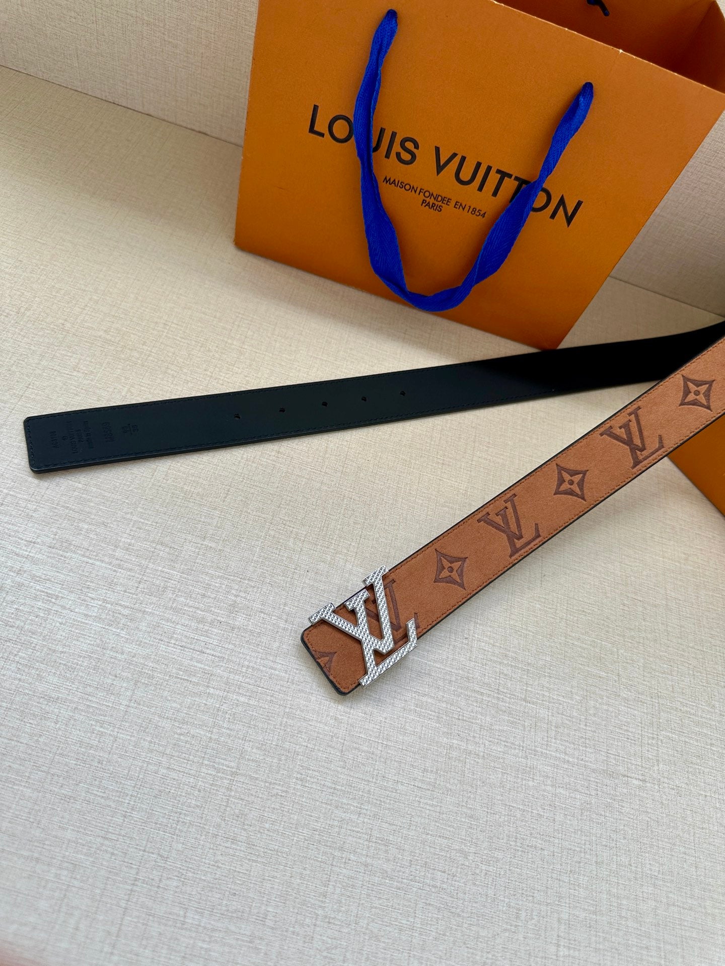 Louis Vuitton monogram belt laid flat, tan strap with gold-tone buckle and dark blue back