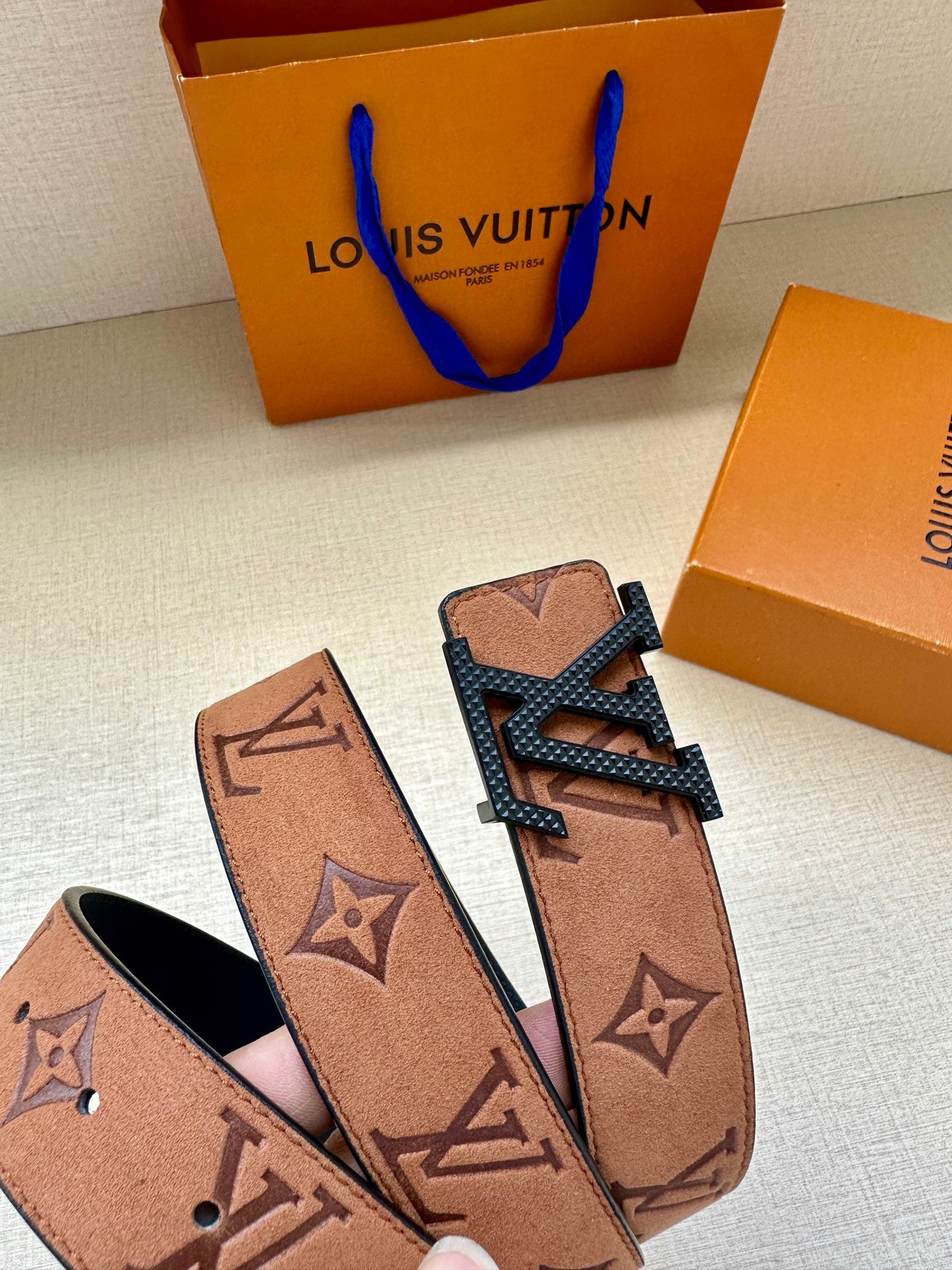 Louis Vuitton belt close-up: tan monogram strap with gold-tone buckle, belt ends