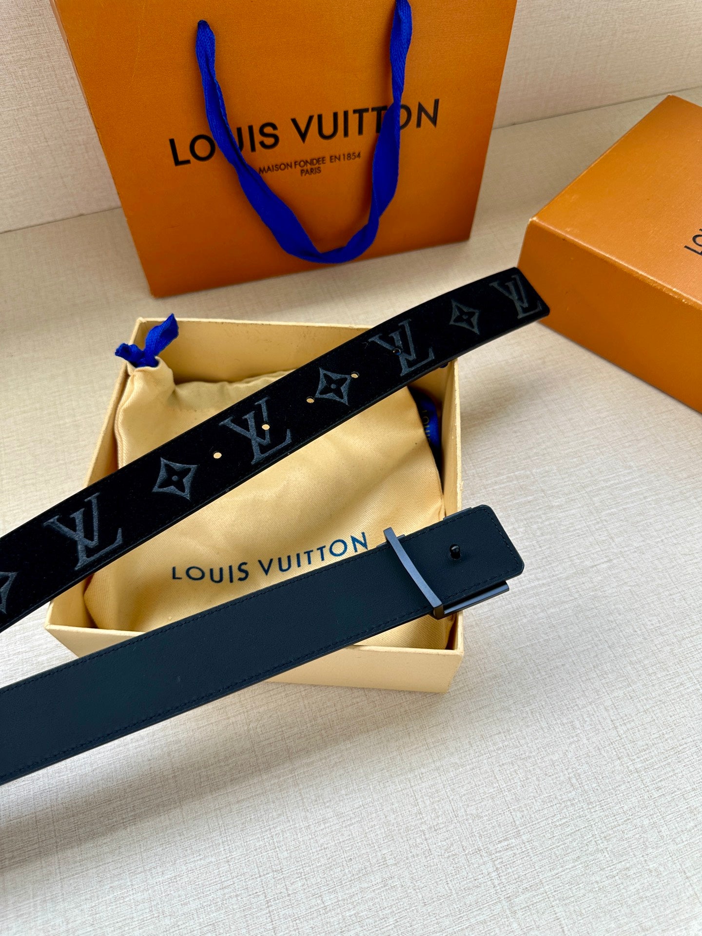 Dark blue monogram belt with silver LV buckle and black strap; buckle sits on leather end.