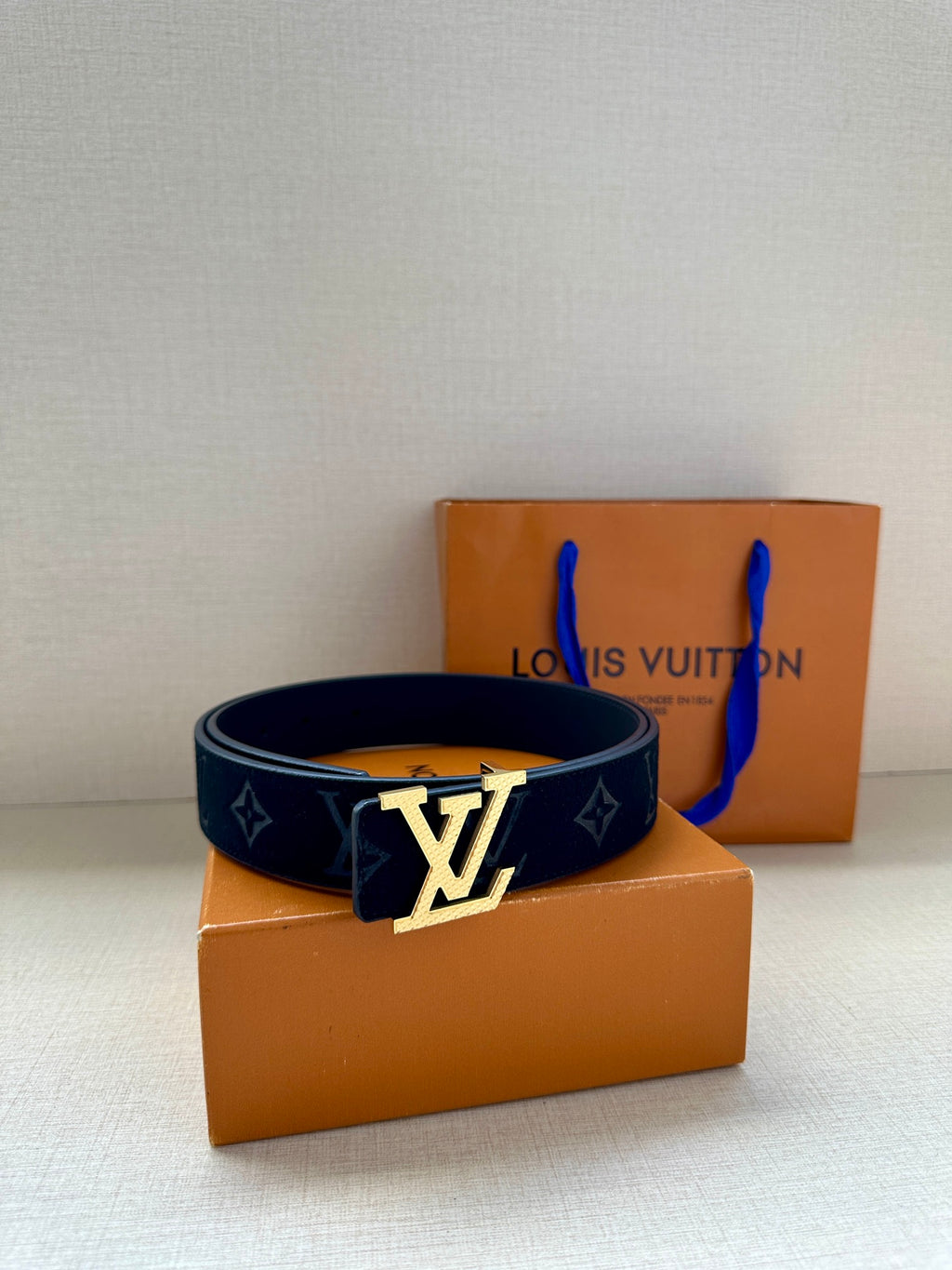 Dark blue patterned belt with silver LV logo buckle; belt looped and centered.