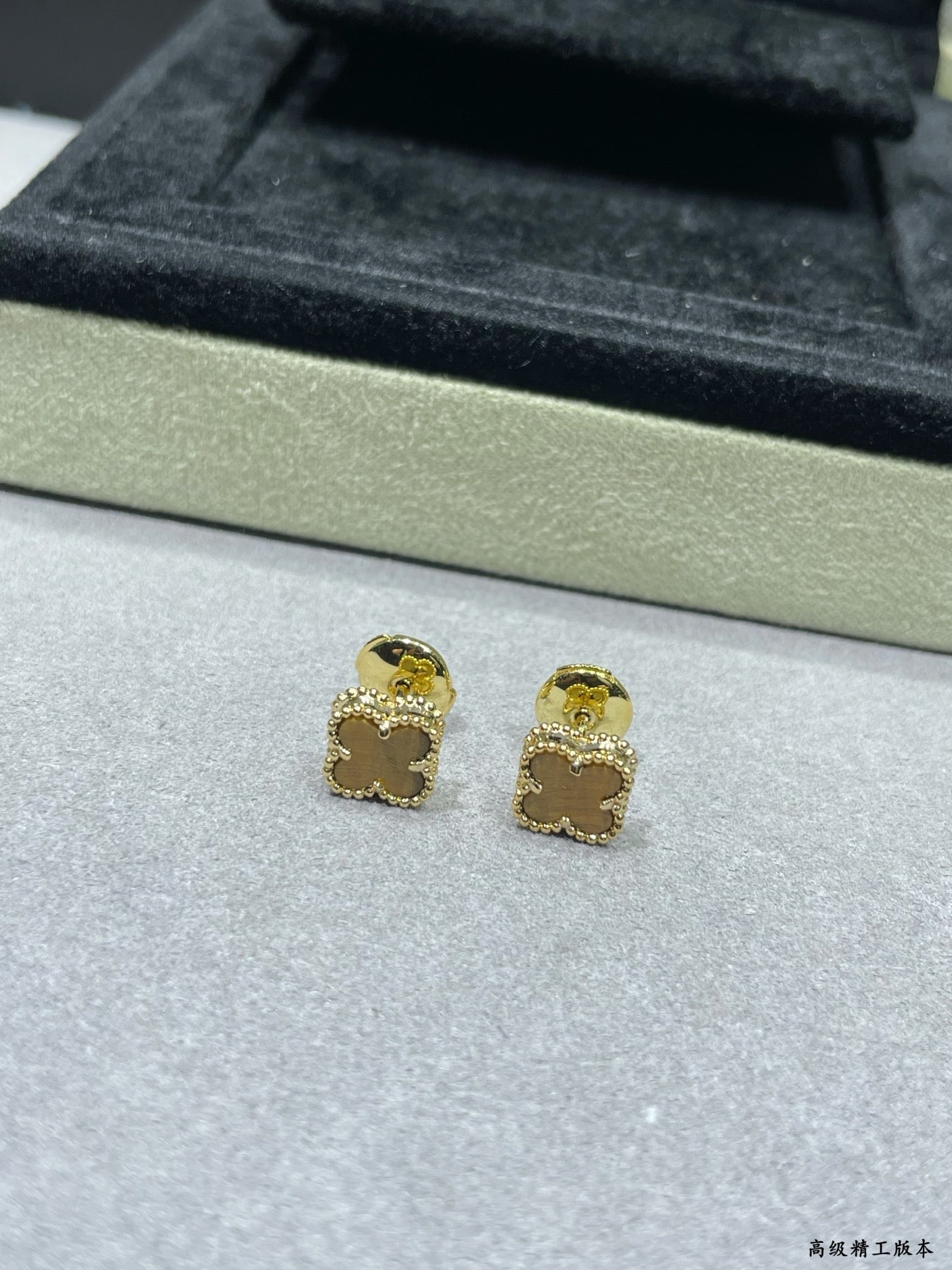 Gold-tone clover stud earrings on display tray