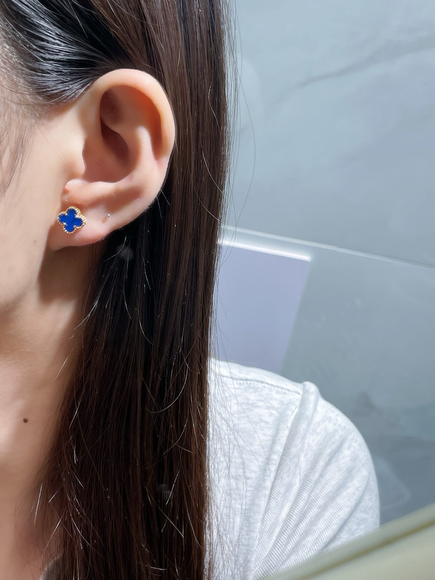 Clover enamel stud earrings on ear with blue centers and gold-tone posts