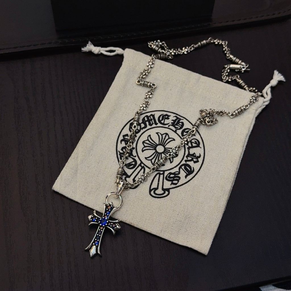 Silver cross pendant necklace with blue stone accents on a drawstring pouch