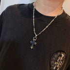 Silver cross pendant necklace with blue enamel charm on a dark crewneck shirt