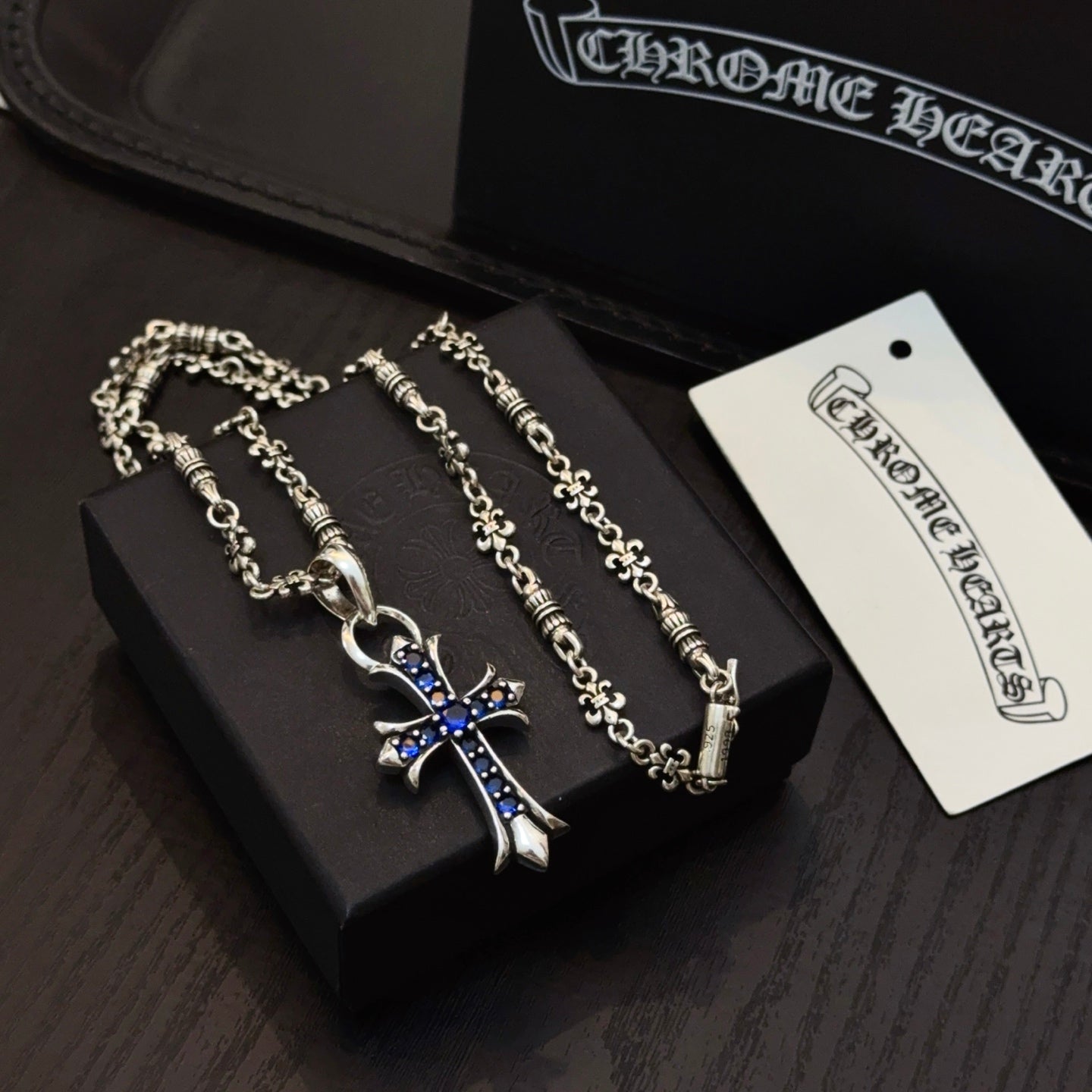 Silver cross pendant necklace with blue enamel charm displayed in a box