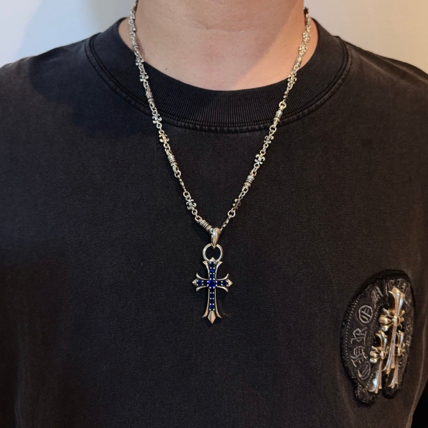 Silver cross pendant necklace with blue enamel charm worn on a black shirt
