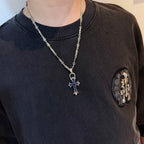 Silver cross pendant necklace with blue enamel charm worn on a dark shirt