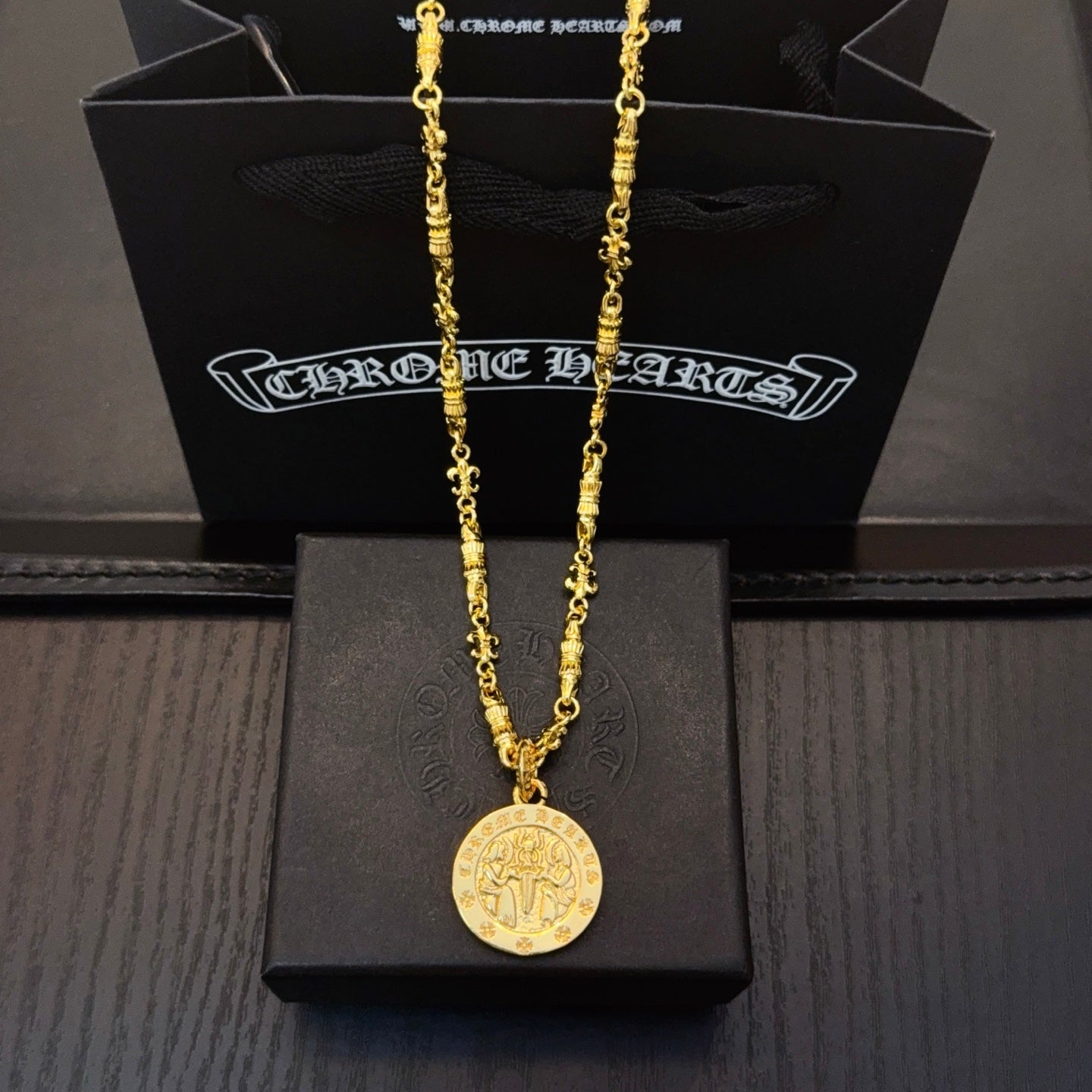 Gold-tone long necklace with round coin pendant on black jewelry box