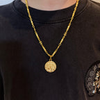 Gold-tone coin pendant necklace worn on dark crewneck shirt