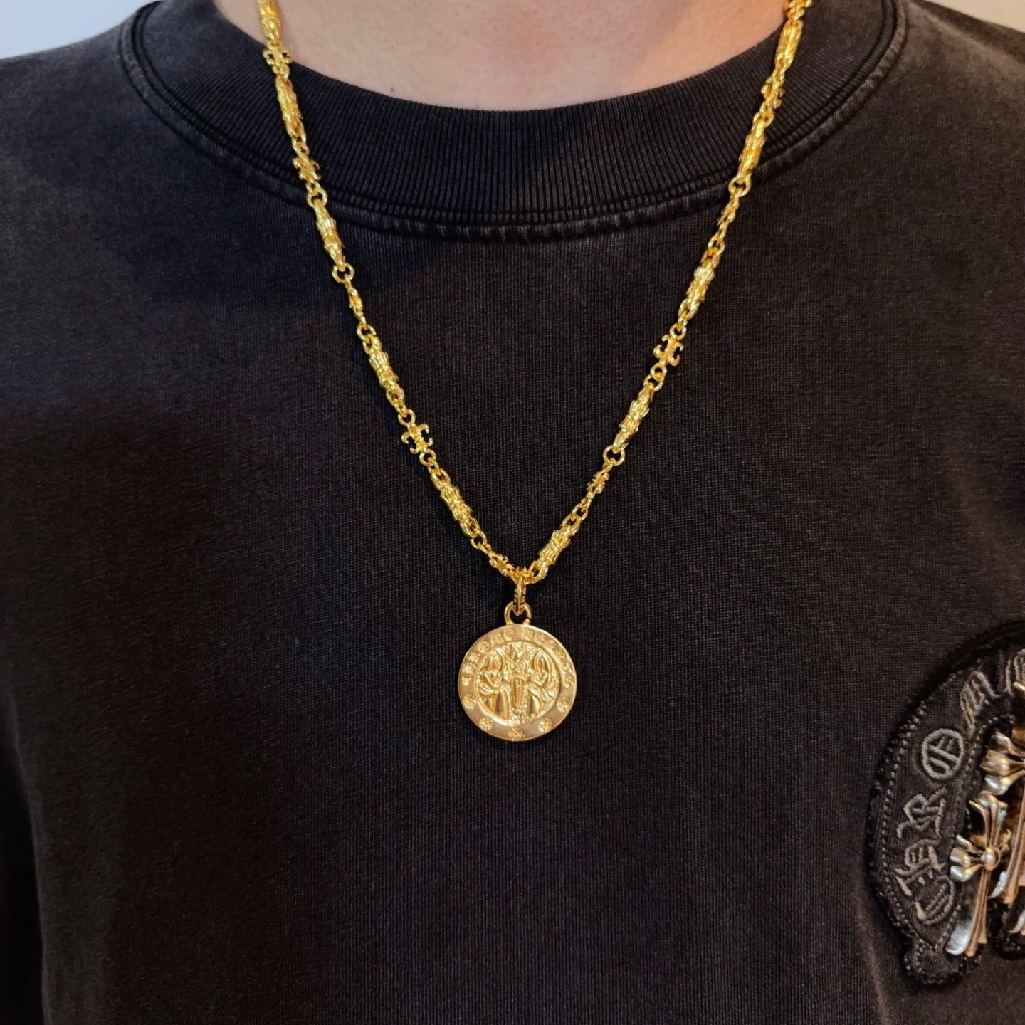 Gold-tone coin pendant necklace worn on dark crewneck shirt