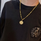 Gold-tone coin pendant necklace worn on dark crewneck shirt with patch