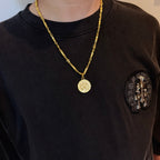 Gold-tone coin pendant necklace worn on dark crewneck shirt